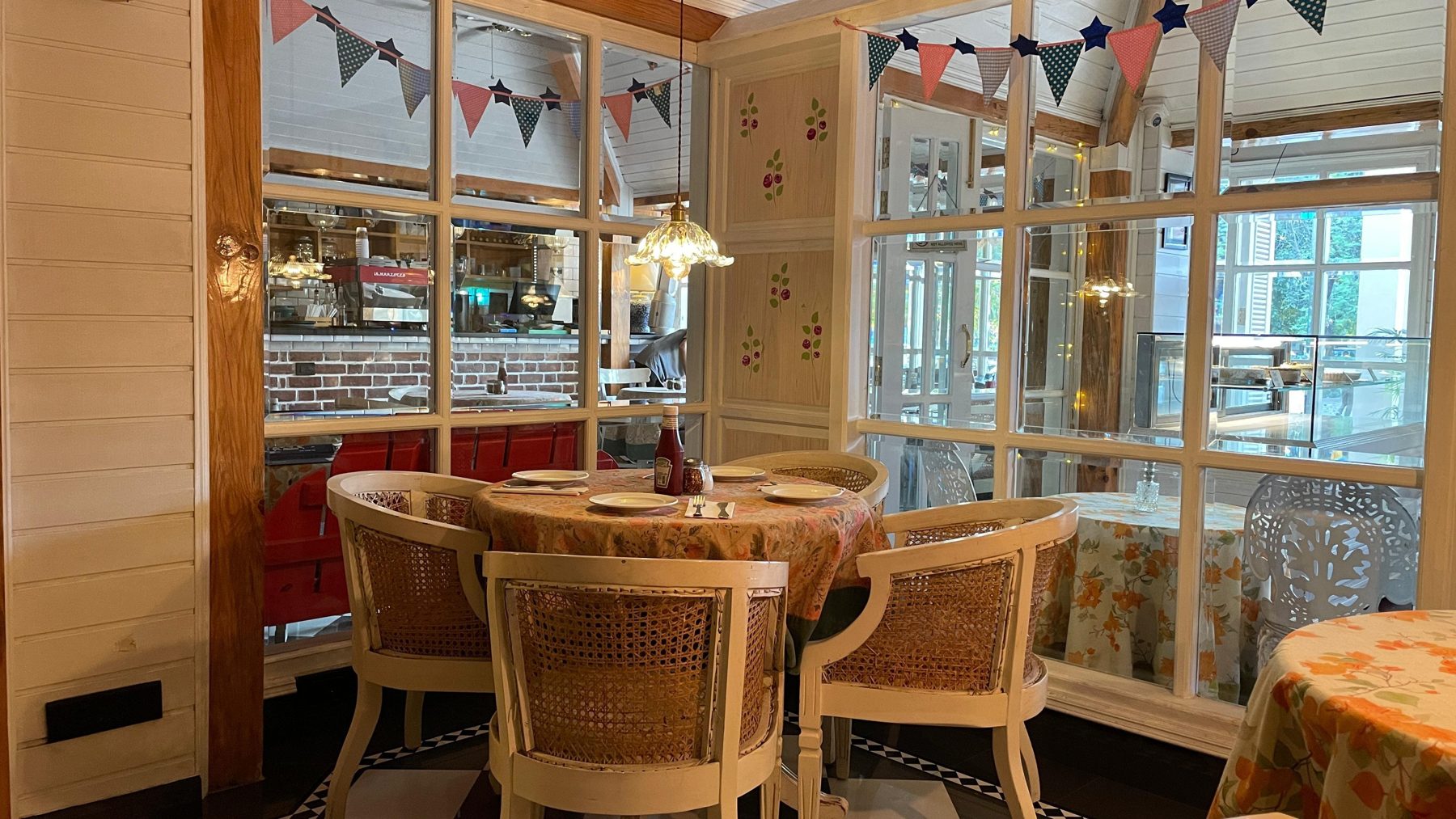 Cane chairs at a set table by the tall windows of Café De Piccolo, bunting above.