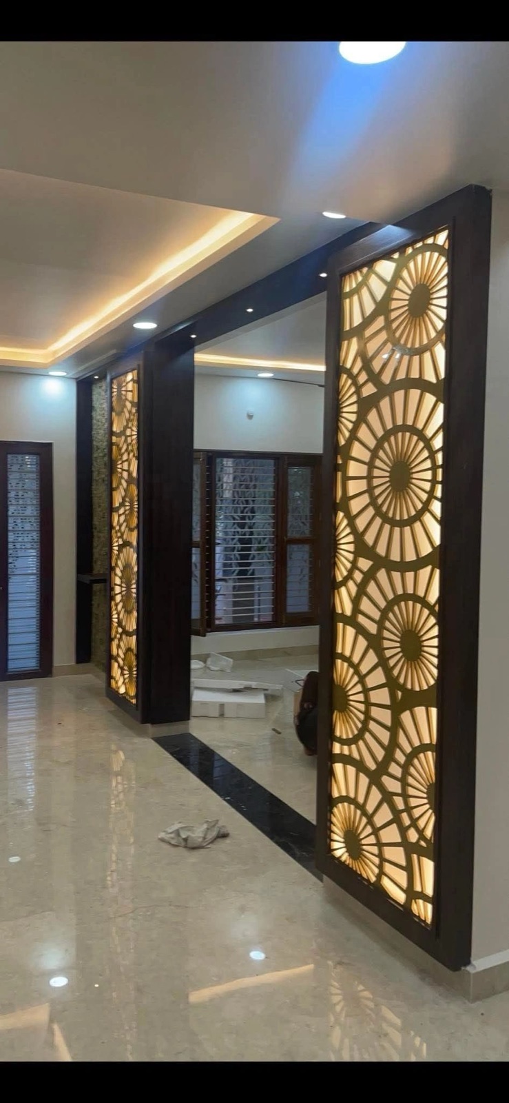 Two tall CNC jaali partitions in dark frames, lit from behind so the circles glow amber.