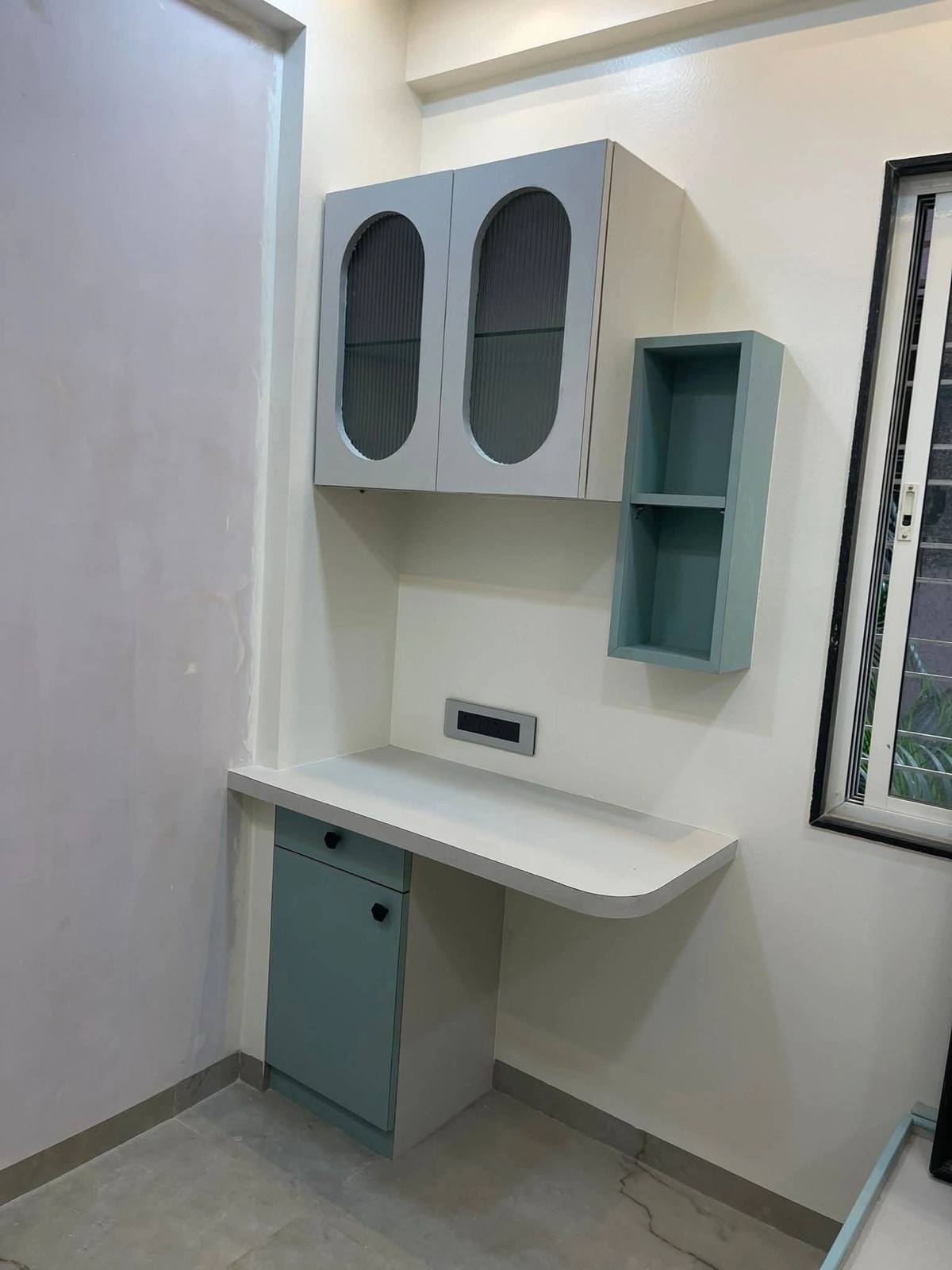 A compact study desk with a curved top, a sage-green drawer unit and two cabinets with oval fluted-glass shutters.